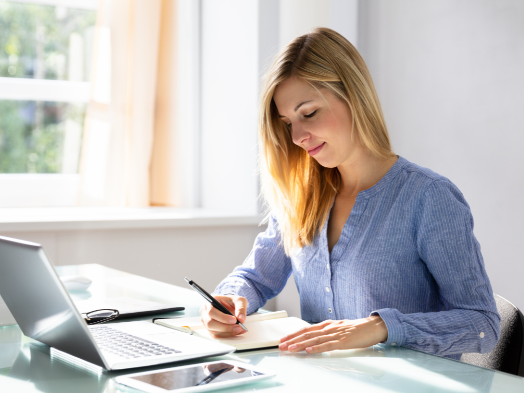 A person making plans using a laptop, a notebook, and a pen.